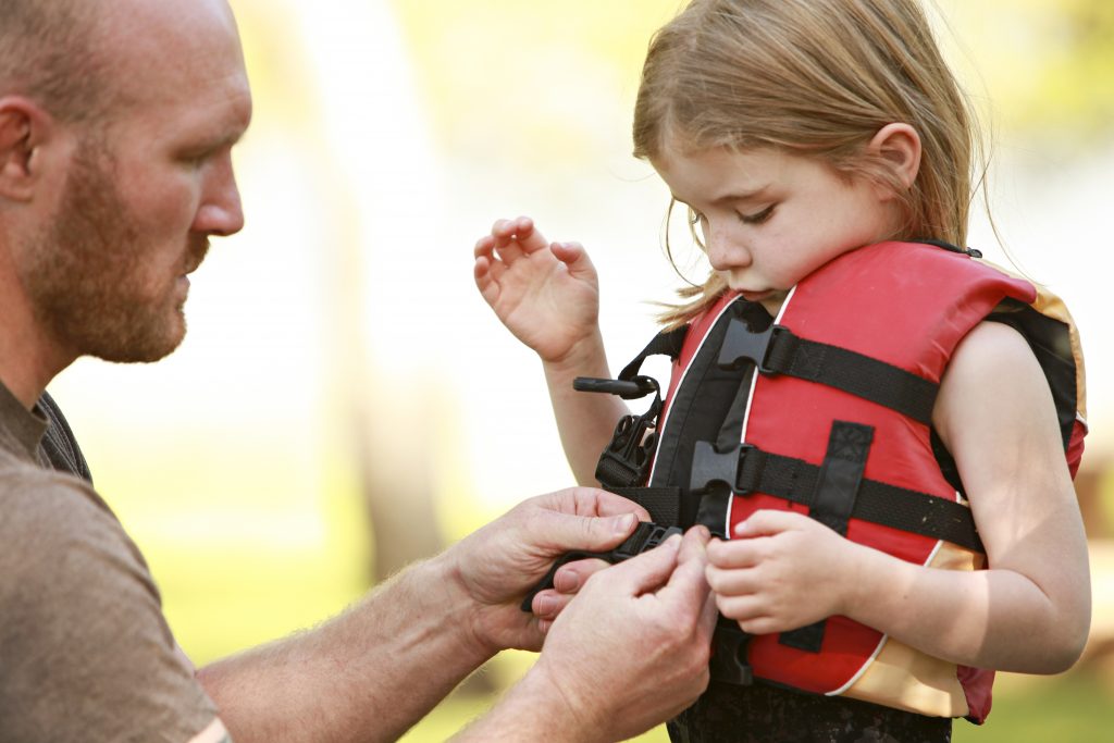 A man helps a young girl clip on her personal flotation device (PFD)/lifejacket